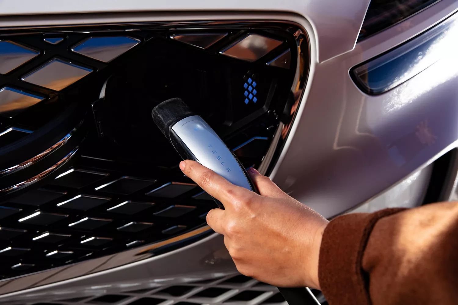 Close up of hand holding charger to charging port on the grille of Genesis Electrified GV70