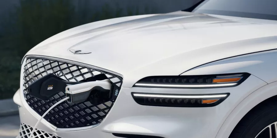 3/4 front driver side close-up of Genesis Electrified GV70 in Uyuni White charging via grille access