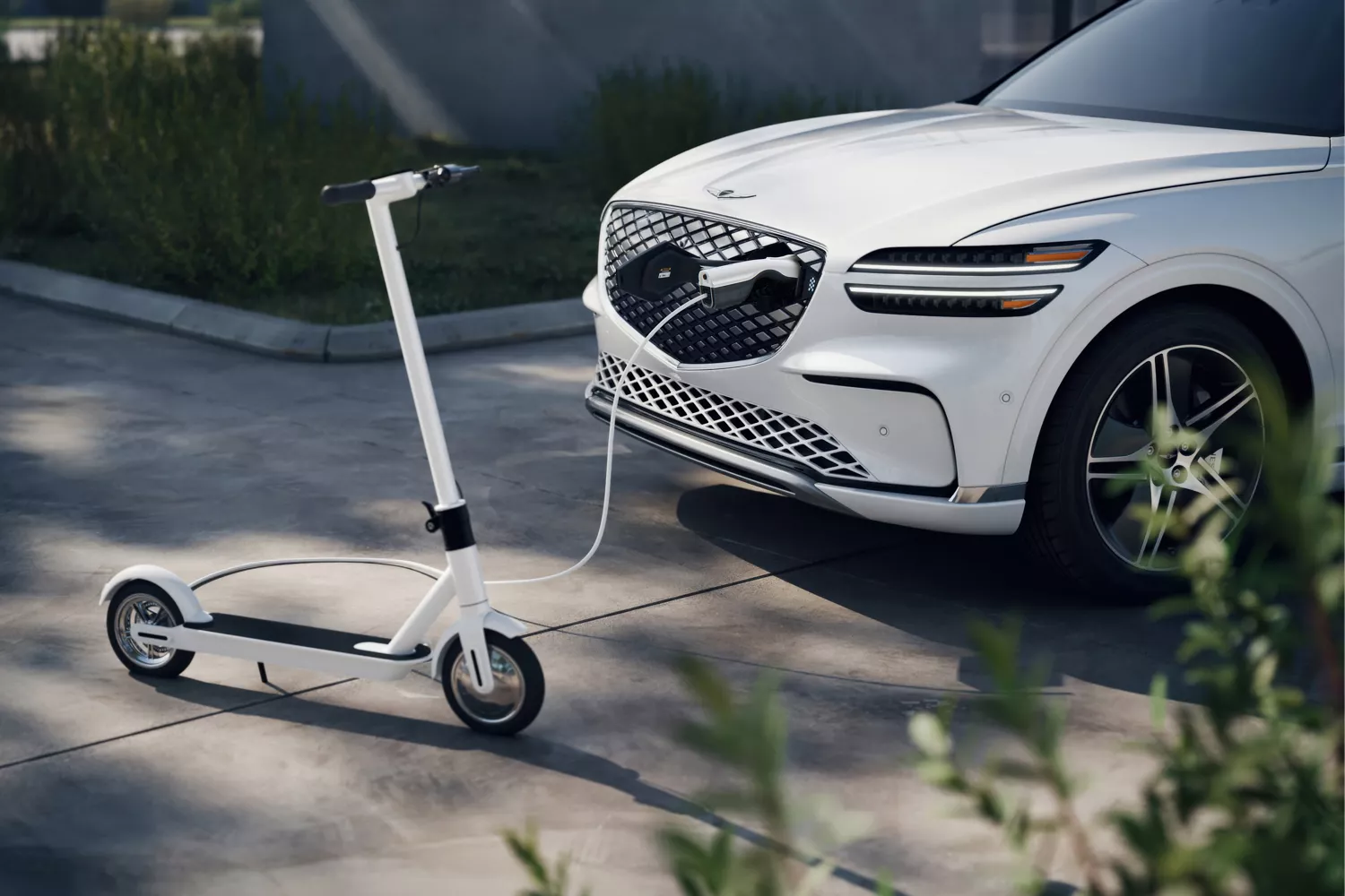 3/4 view of white Genesis Electrified GV70 in driveway charging electric scooter via front port