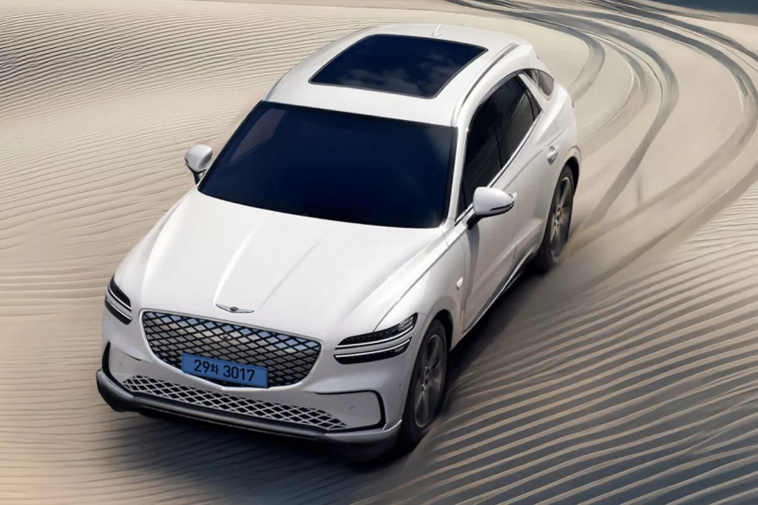 3/4 front driver side aerial view of Genesis Electrified GV70 driving through sand dunes