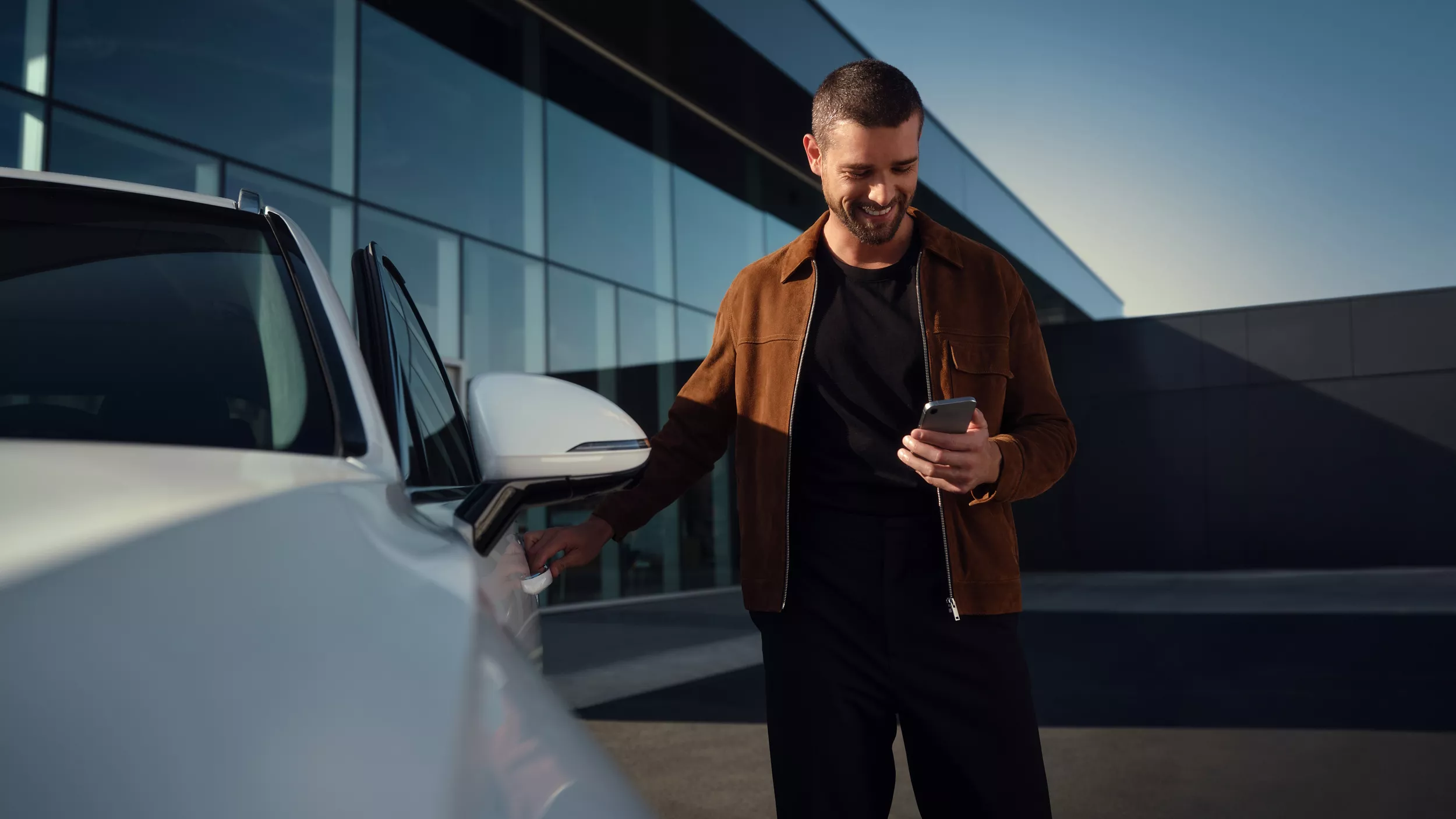 Man holding phone, grasping driver side door handle of Genesis Electrified GV70 in Uyuni White