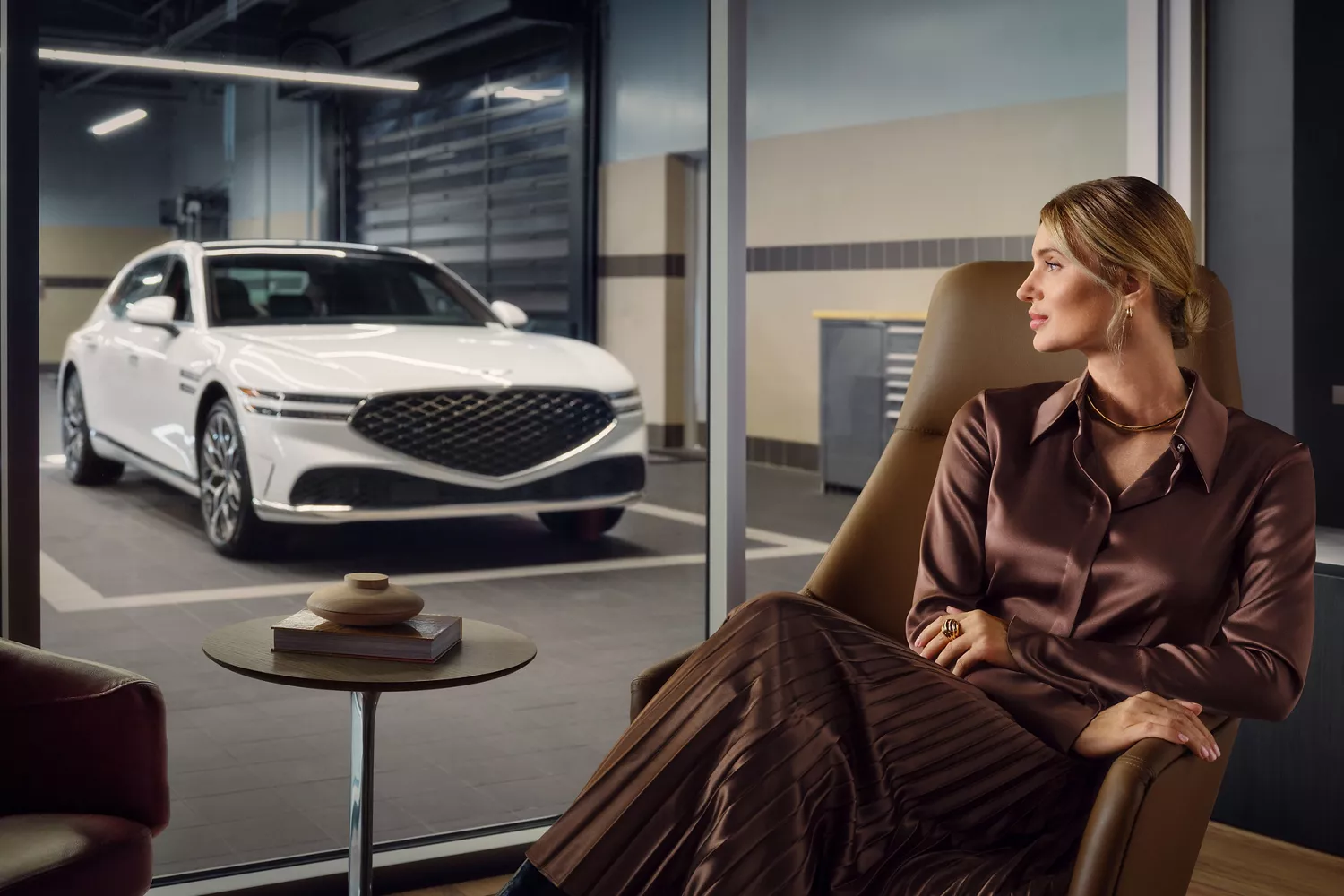 Woman seated in waiting room views white car in garage through glass walls
