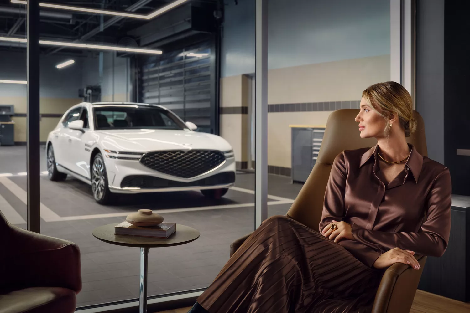 Woman seated in waiting room views white car in garage through glass walls