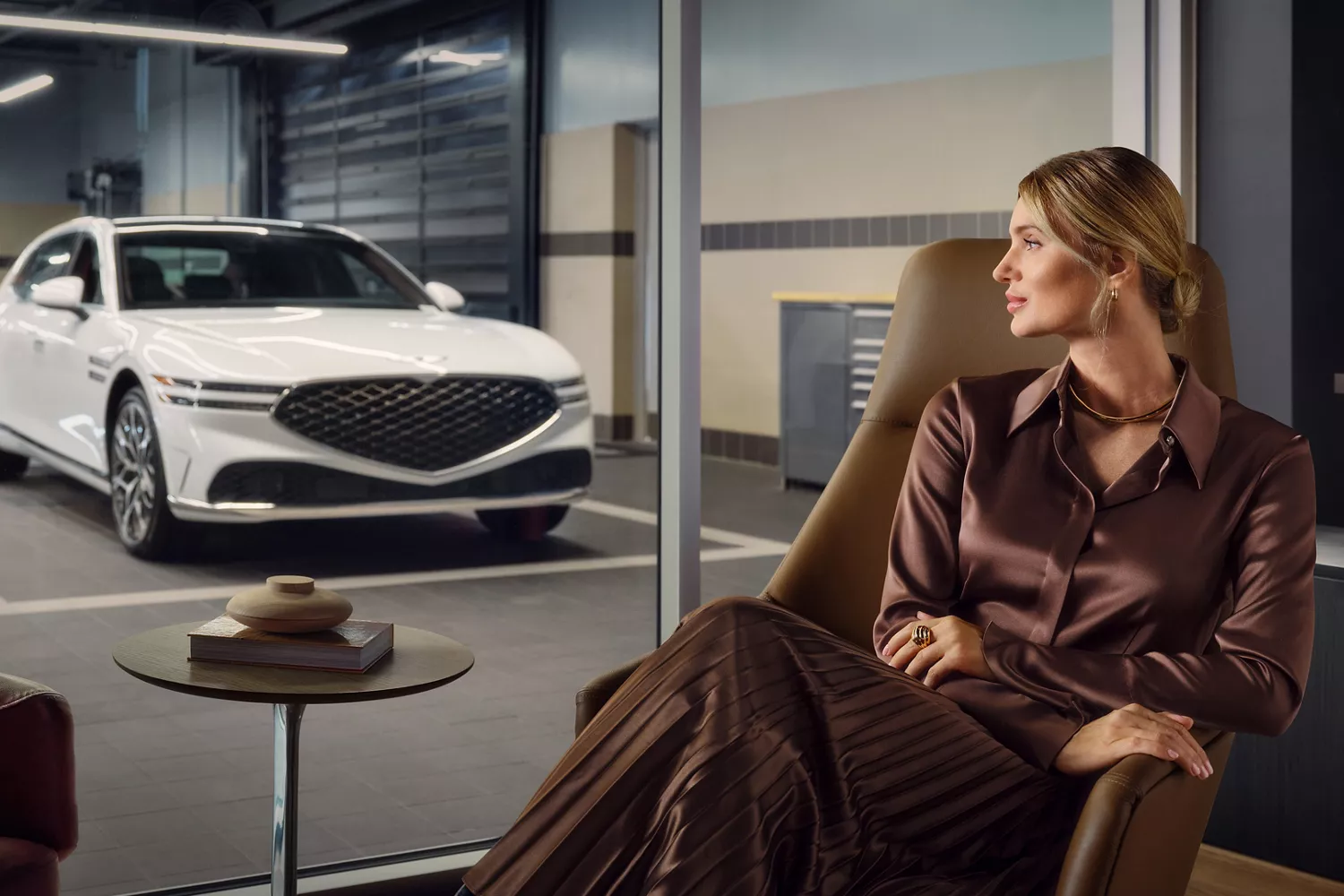 View of Genesis G90 in service center through glass, person seated in waiting area.