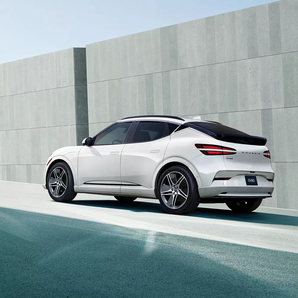 3/4 rear driver side view of 2026 Genesis GV60 in white parked by concrete wall