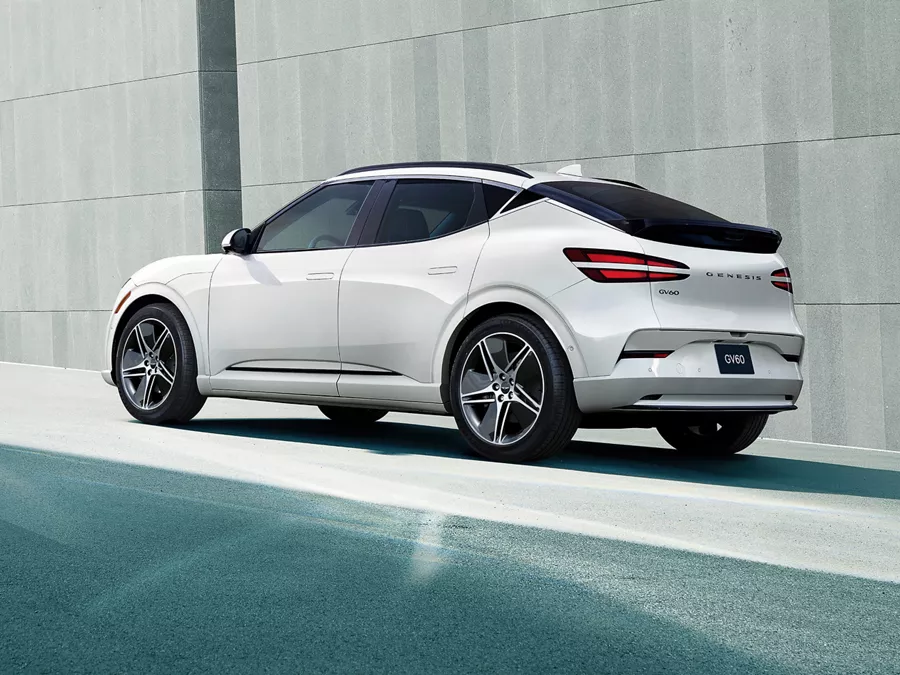 3/4 rear driver side view of 2026 Genesis GV60 in white parked by concrete wall