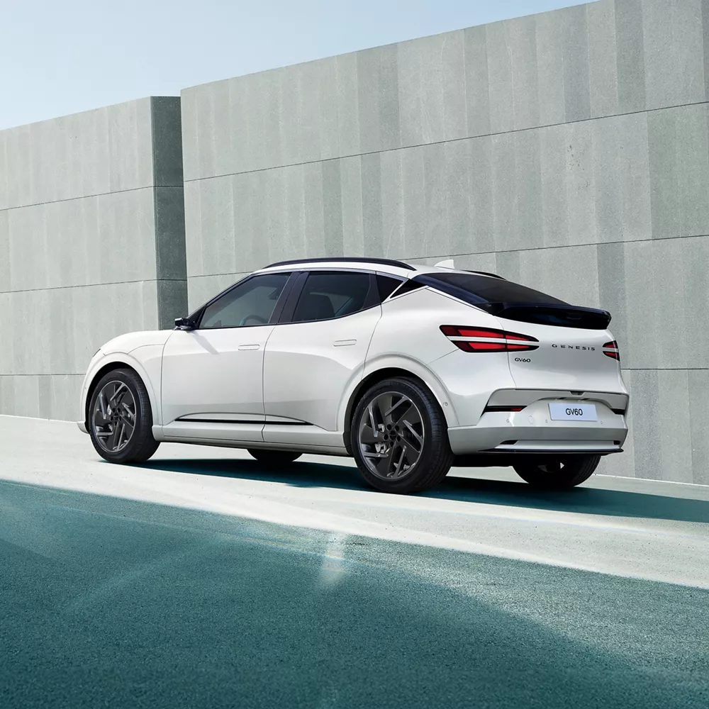 3/4 rear driver side view of 2026 Genesis GV60 in white parked by concrete wall