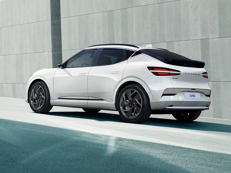 3/4 rear driver side view of 2026 Genesis GV60 in white parked by concrete wall
