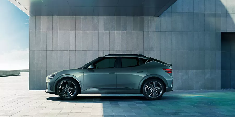 Driver side profile of 2026 Genesis GV60 in Tromso Green park next to modern house