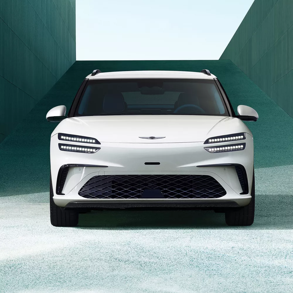 Front view of 2026 Genesis GV60 in white, framed by modern concrete building in the background