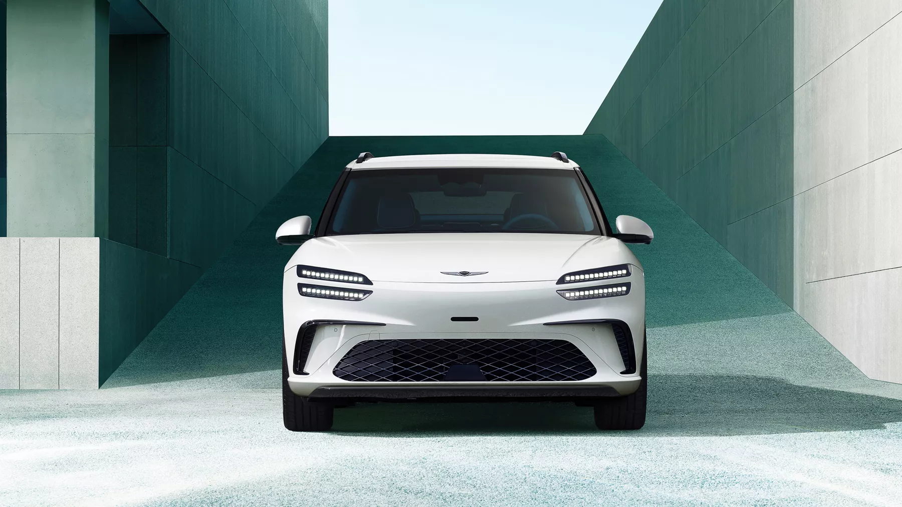 Front view of 2026 Genesis GV60 in white, framed by modern concrete building in the background