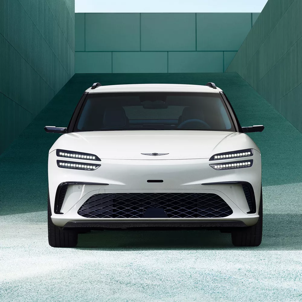 Front view of 2026 Genesis GV60 in white, framed by modern concrete building in the background