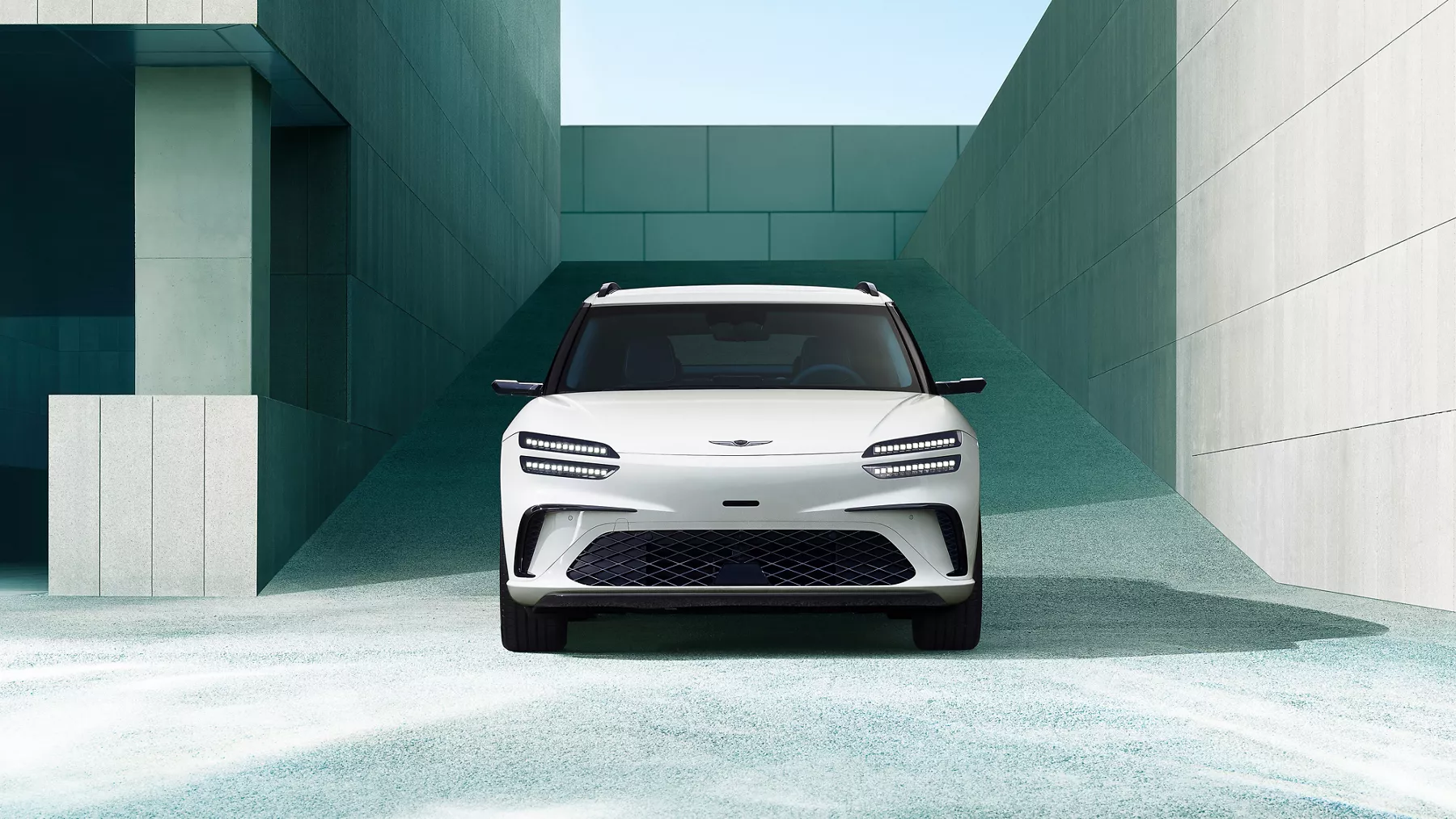 Front view of 2026 Genesis GV60 in white, framed by modern concrete building in the background