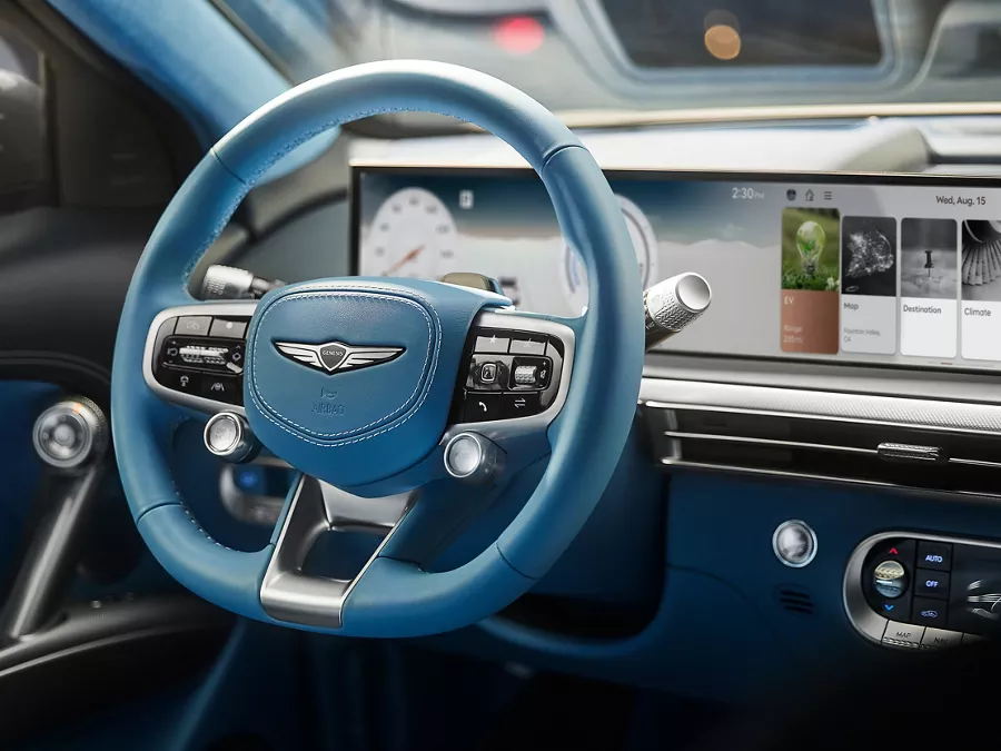 Interior shot of 2026 Genesis GV60 with blue steering wheel and touchscreen infotainment system