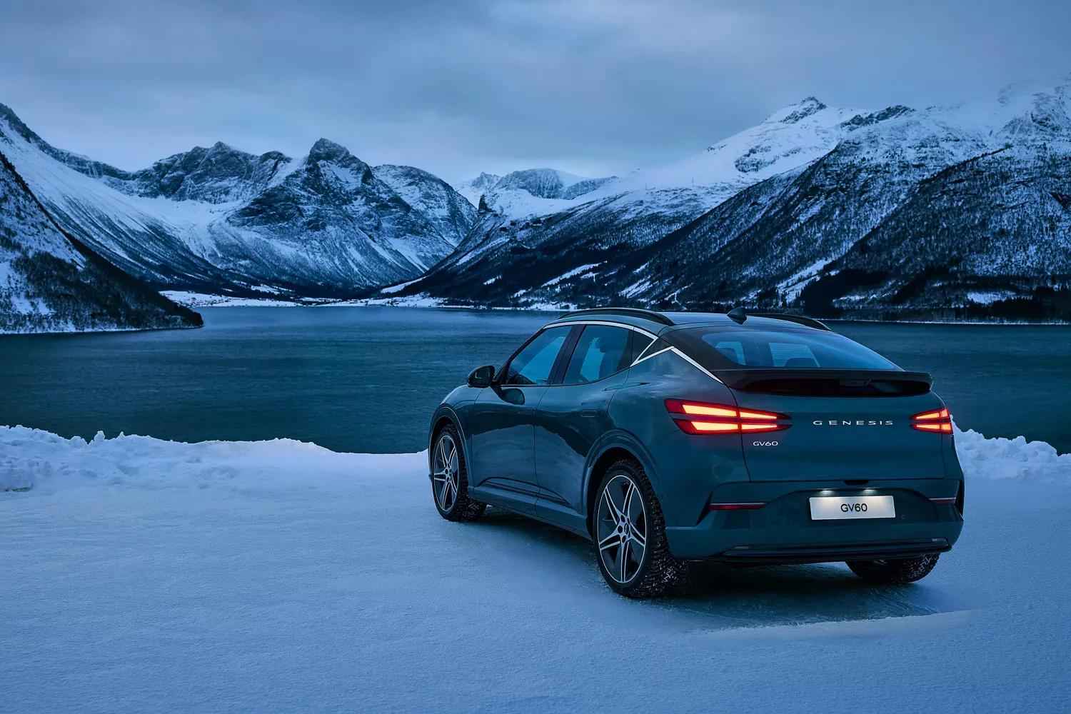 3/4 rear driver side view of 2026 Genesis GV60 parked in front of snowy lake and mountain landscape