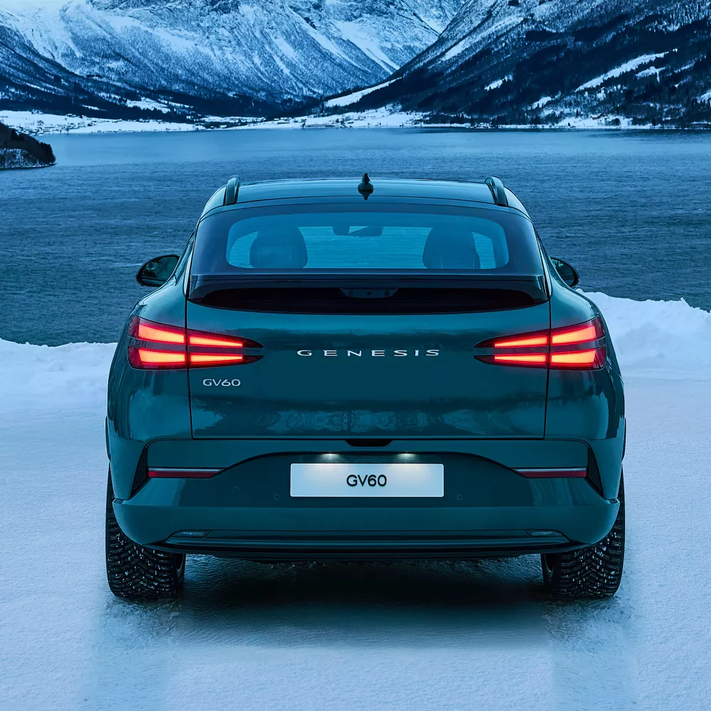 Rear view of 2026 Genesis GV60 parked in front of snowy lake and mountain landscape