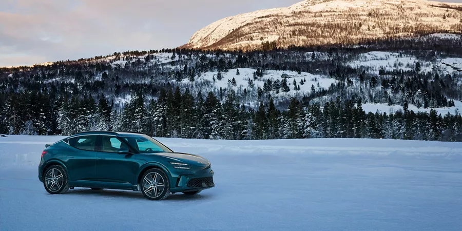 Passenger side profile view of Genesis GV60 parked with snowy mountains in background
