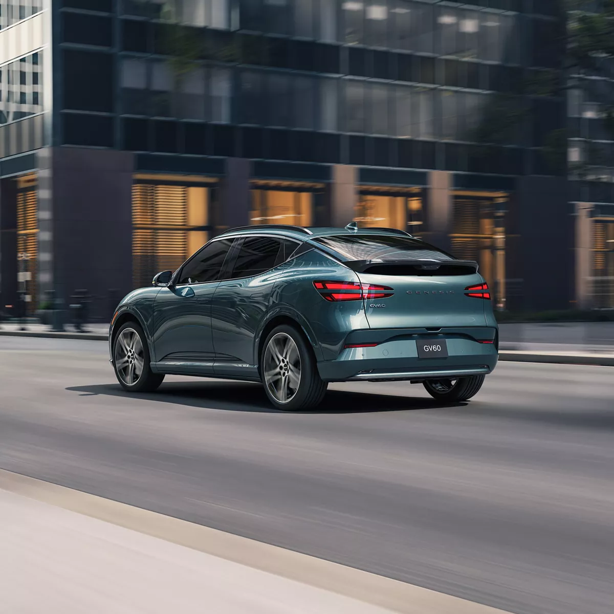 Rear 3/4 driver side view of Genesis GV60 in Tromso Green driving along city street