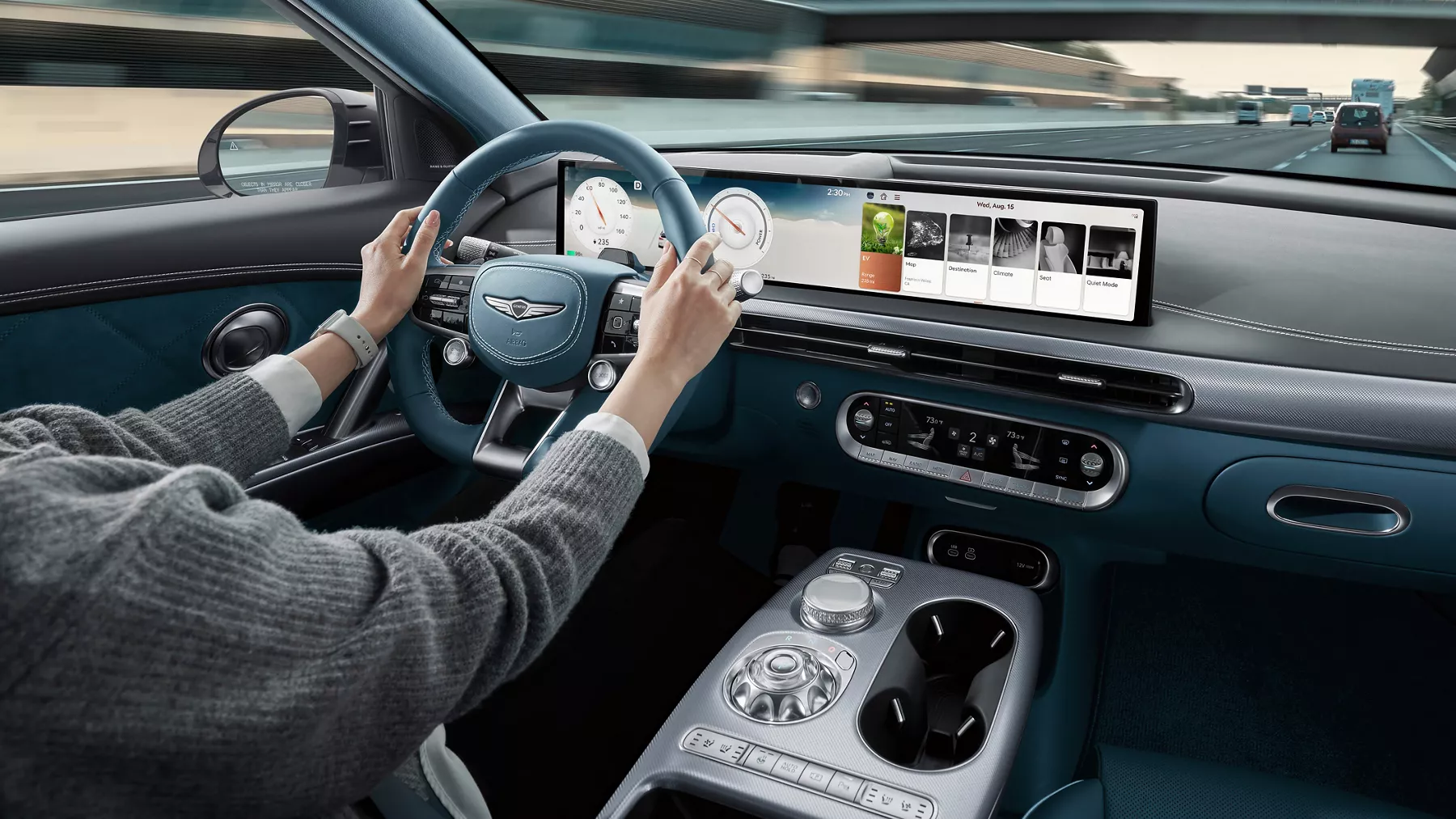 2026 Genesis GV60 interior from driver’s view with blue wheel, digital dash, and highway ahead