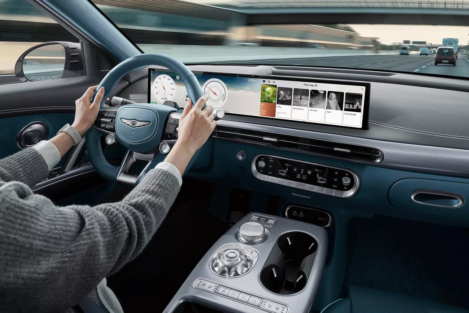 2026 Genesis GV60 interior from driver’s view with blue wheel, digital dash, and highway ahead