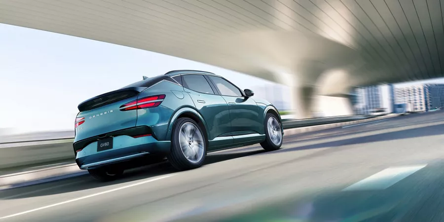 3/4 rear passenger side view of 2026 Genesis GV60 in Tromso Green driving under modern bridge