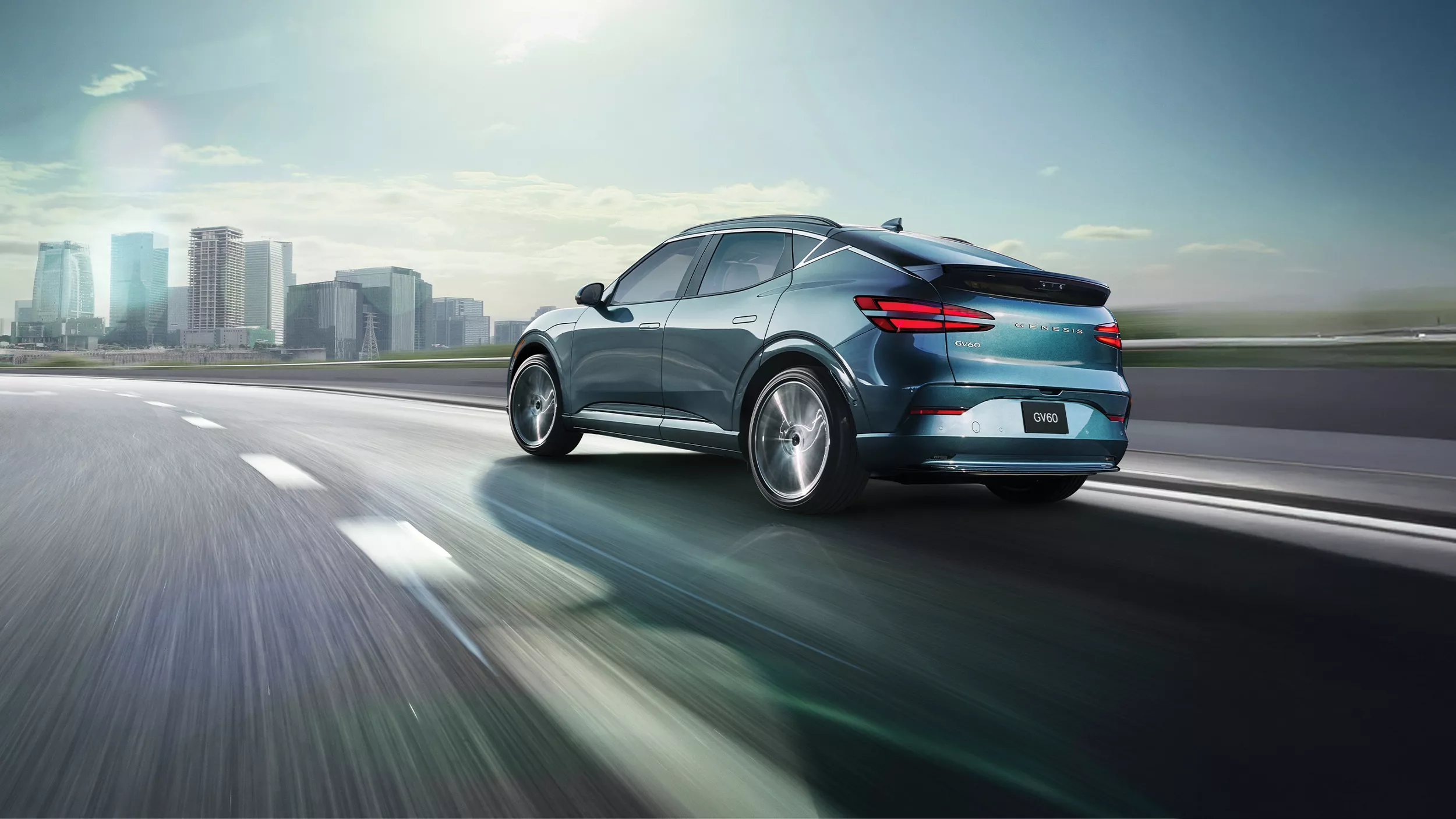 3/4 rear driver side view of 2026 Genesis GV60 in Tromso Green driving on city skyline highway