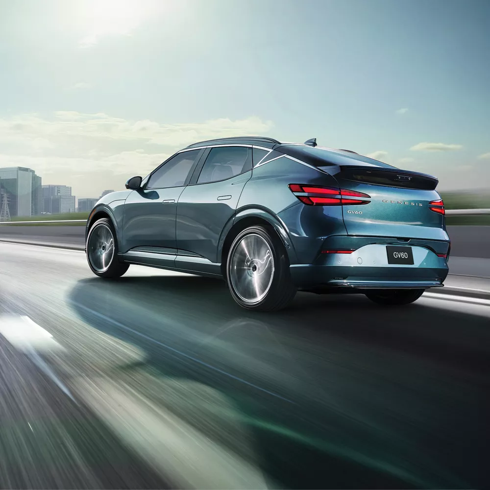 3/4 rear driver side view of 2026 Genesis GV60 in Tromso Green driving on city skyline highway