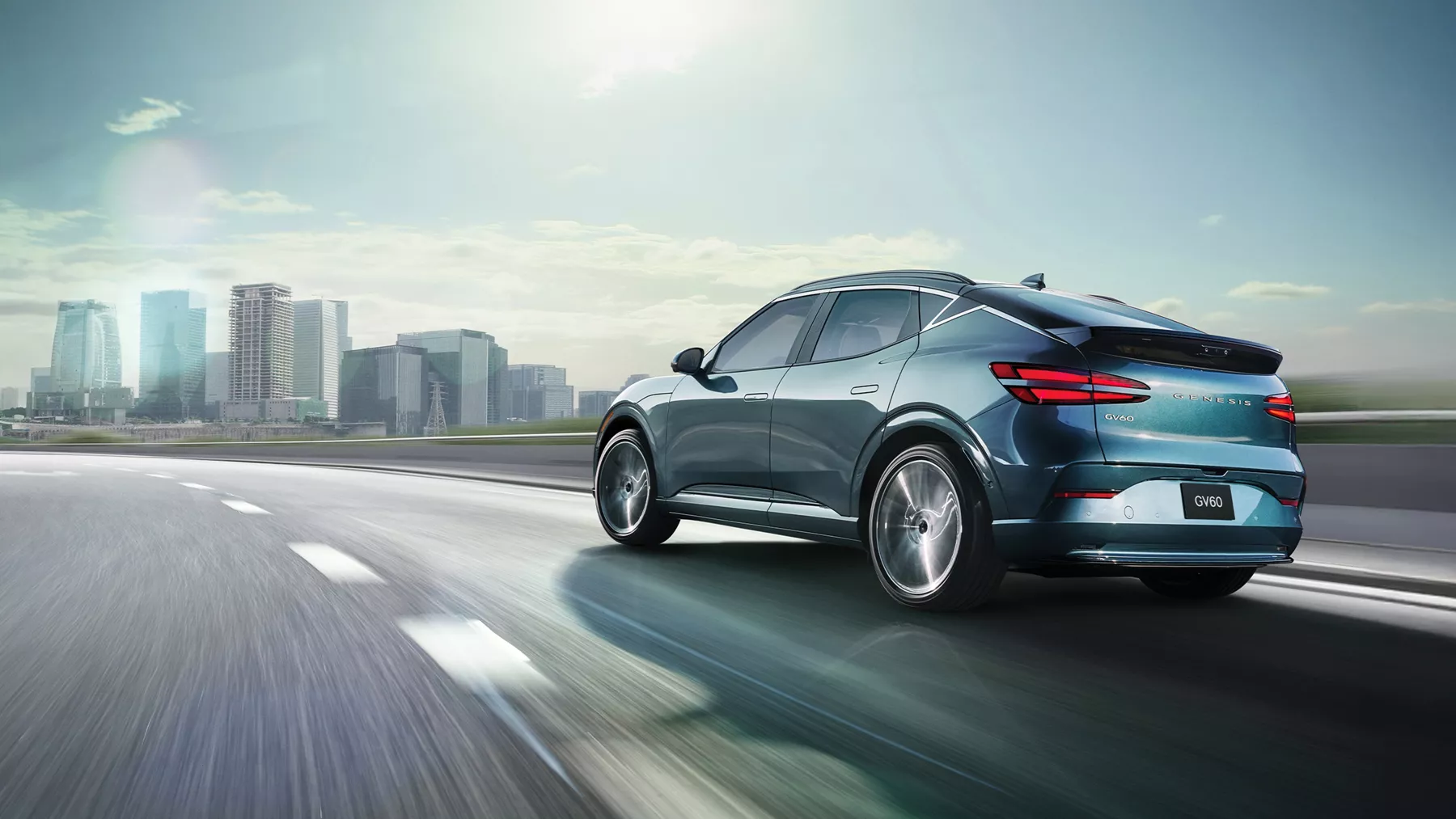 3/4 rear driver side view of 2026 Genesis GV60 in Tromso Green driving on city skyline highway
