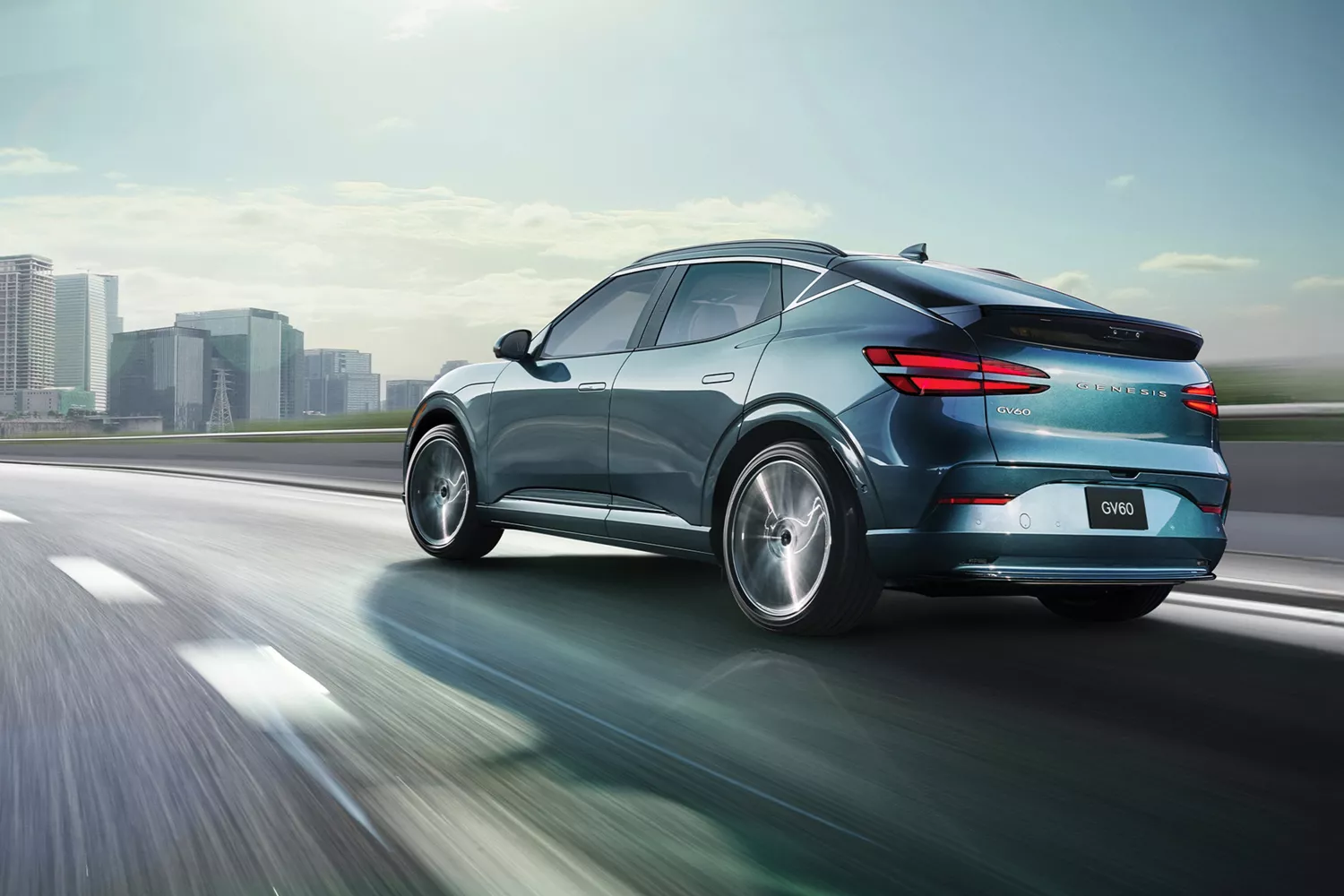 3/4 rear driver side view of 2026 Genesis GV60 in Tromso Green driving on city skyline highway