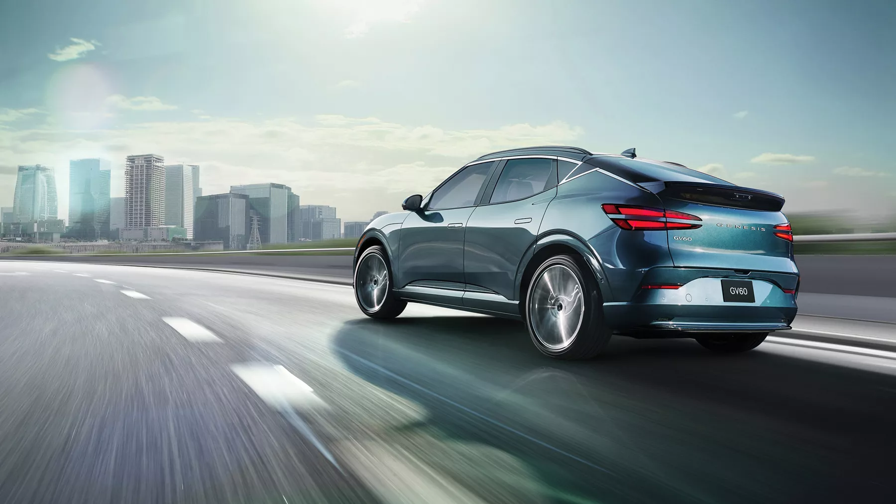 3/4 rear driver's side view of 2026 Genesis GV60 driving along highway towards city skyline