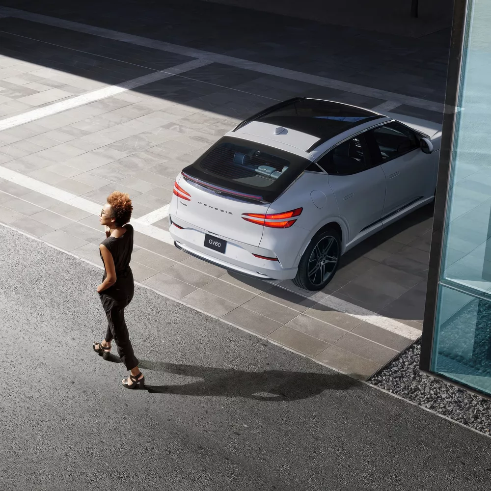 Rear view of Genesis GV60 parked as woman walks behind, highlighting rear collision avoidance feature