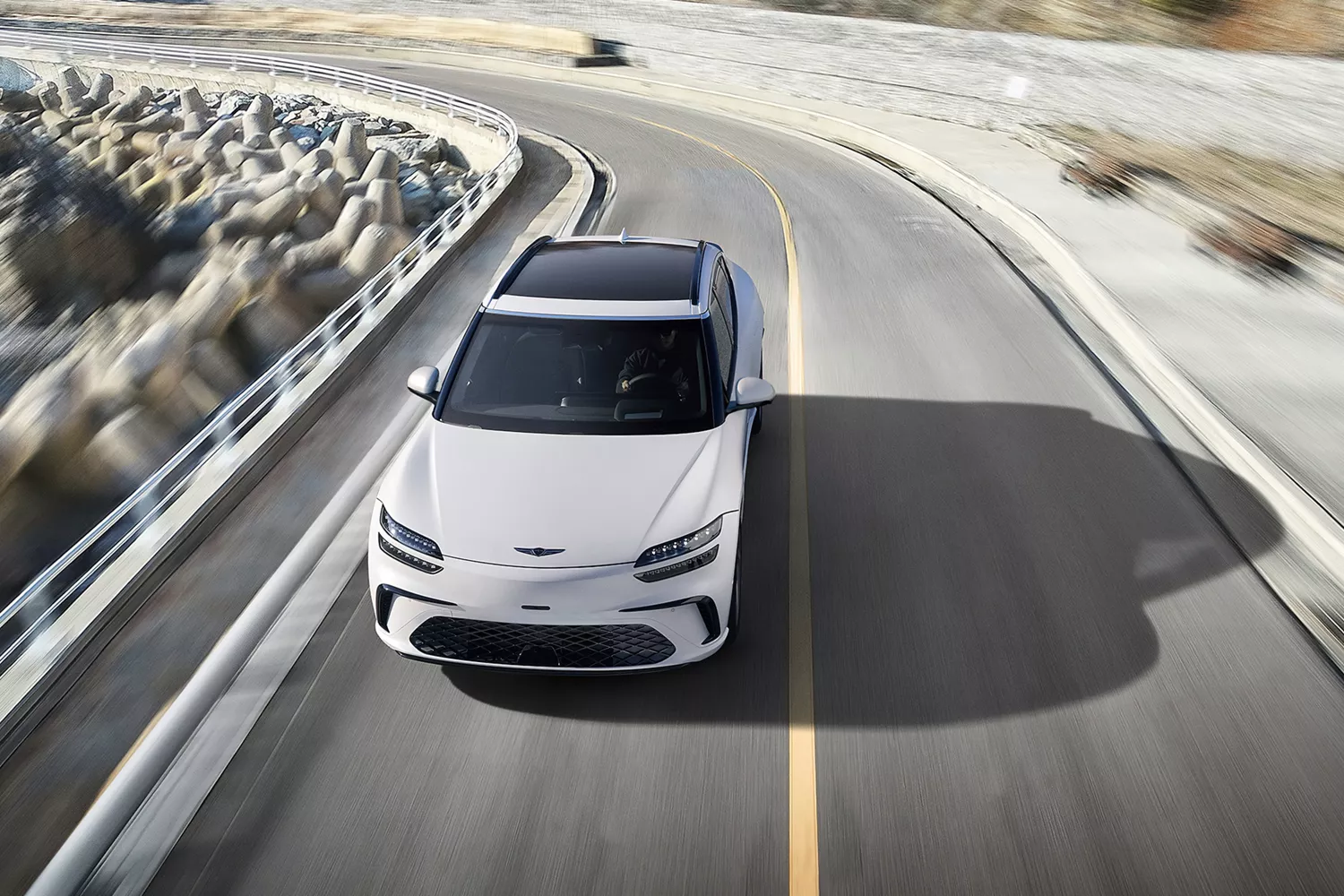 Front aerial view of 2026 Genesis GV60 in white driving on coastal road