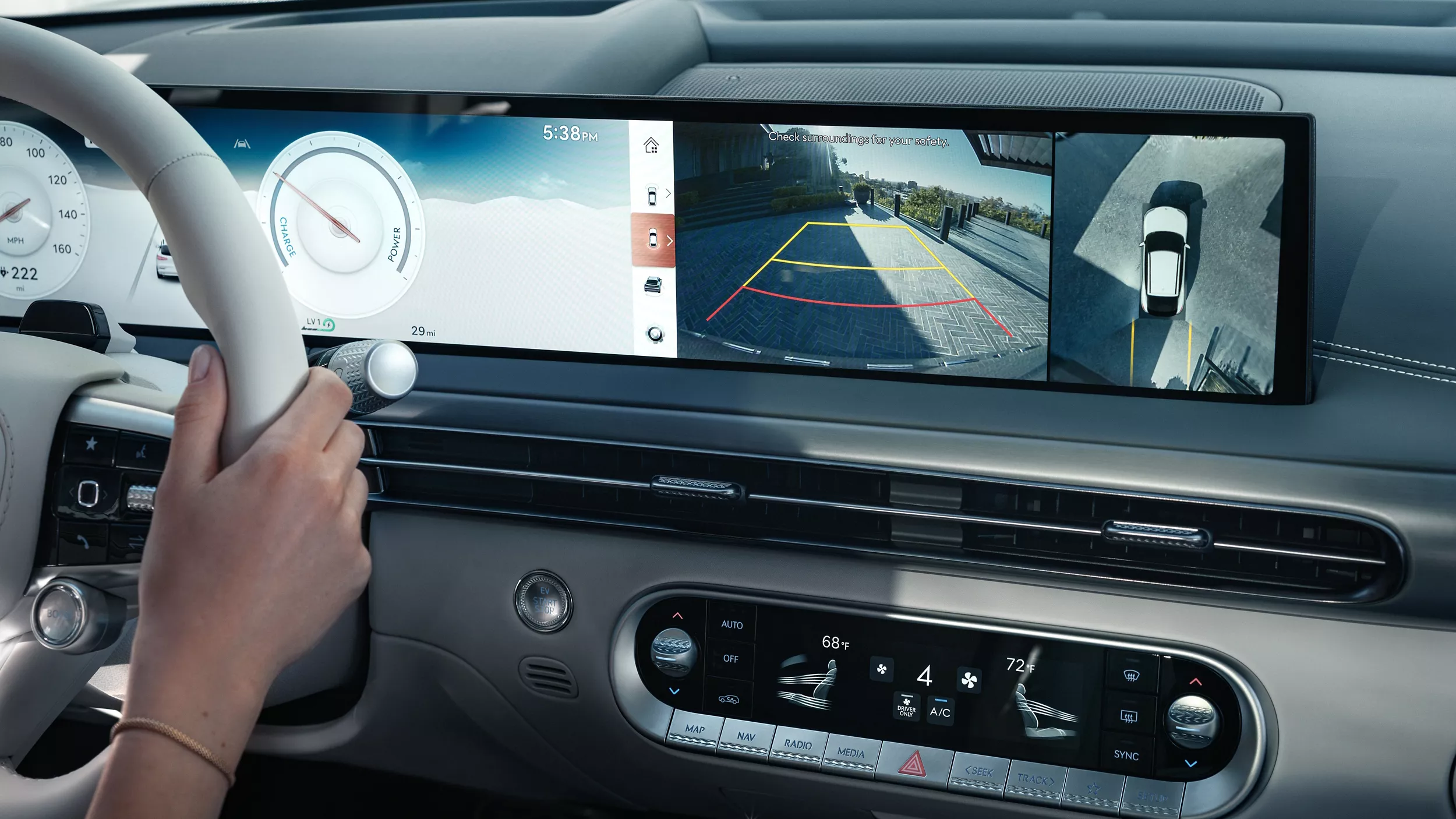 Interior close-up of hand on steering wheel, rear camera shown on OLED display, inside Genesis GV60