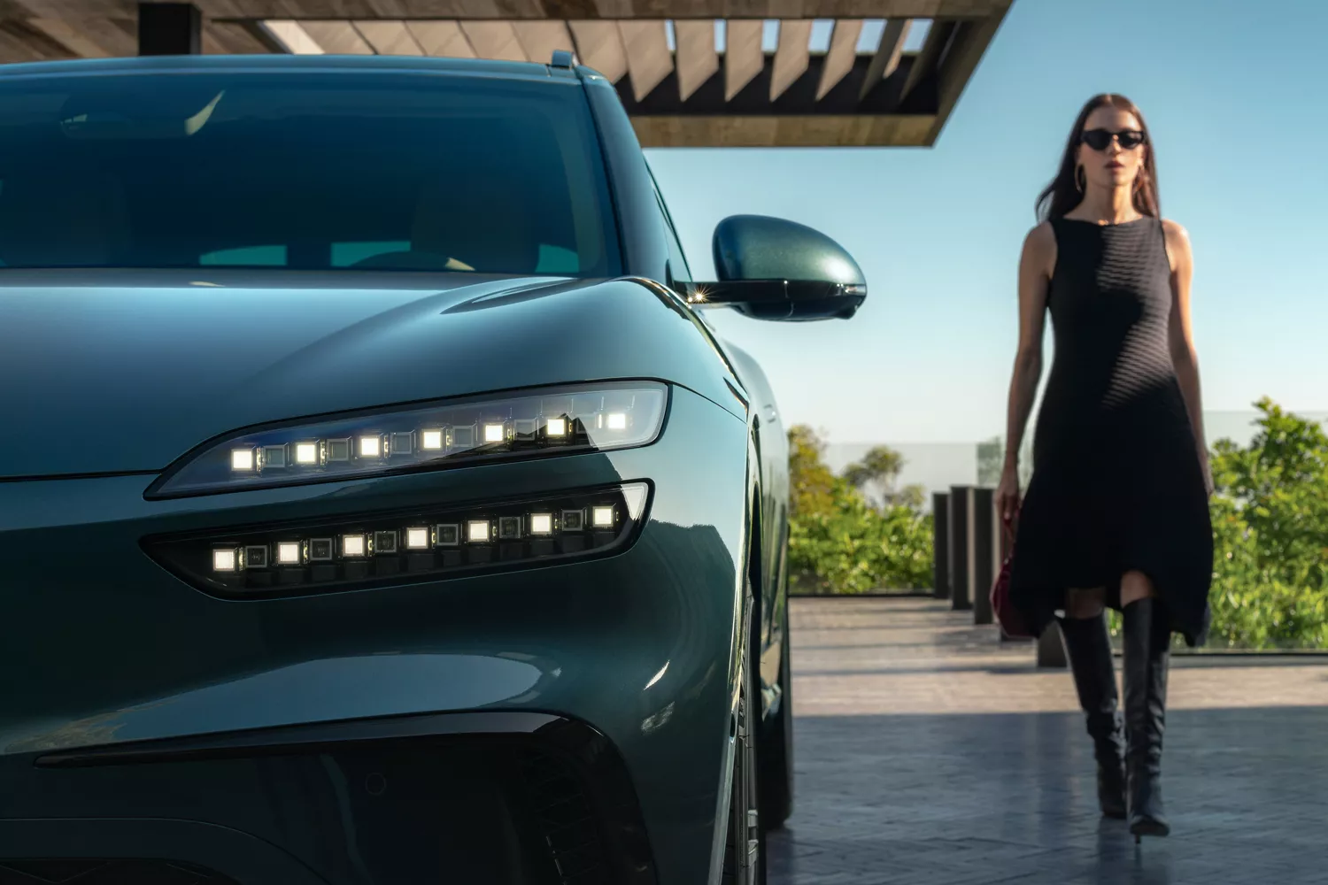 Front view of driver side headlight details on Genesis GV60 in Tromso Green, woman walking beside