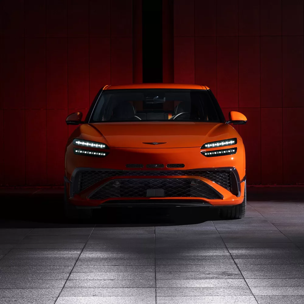 Front facing view of 2027 Genesis GV60 Magma in orange parked in dimly lit garage