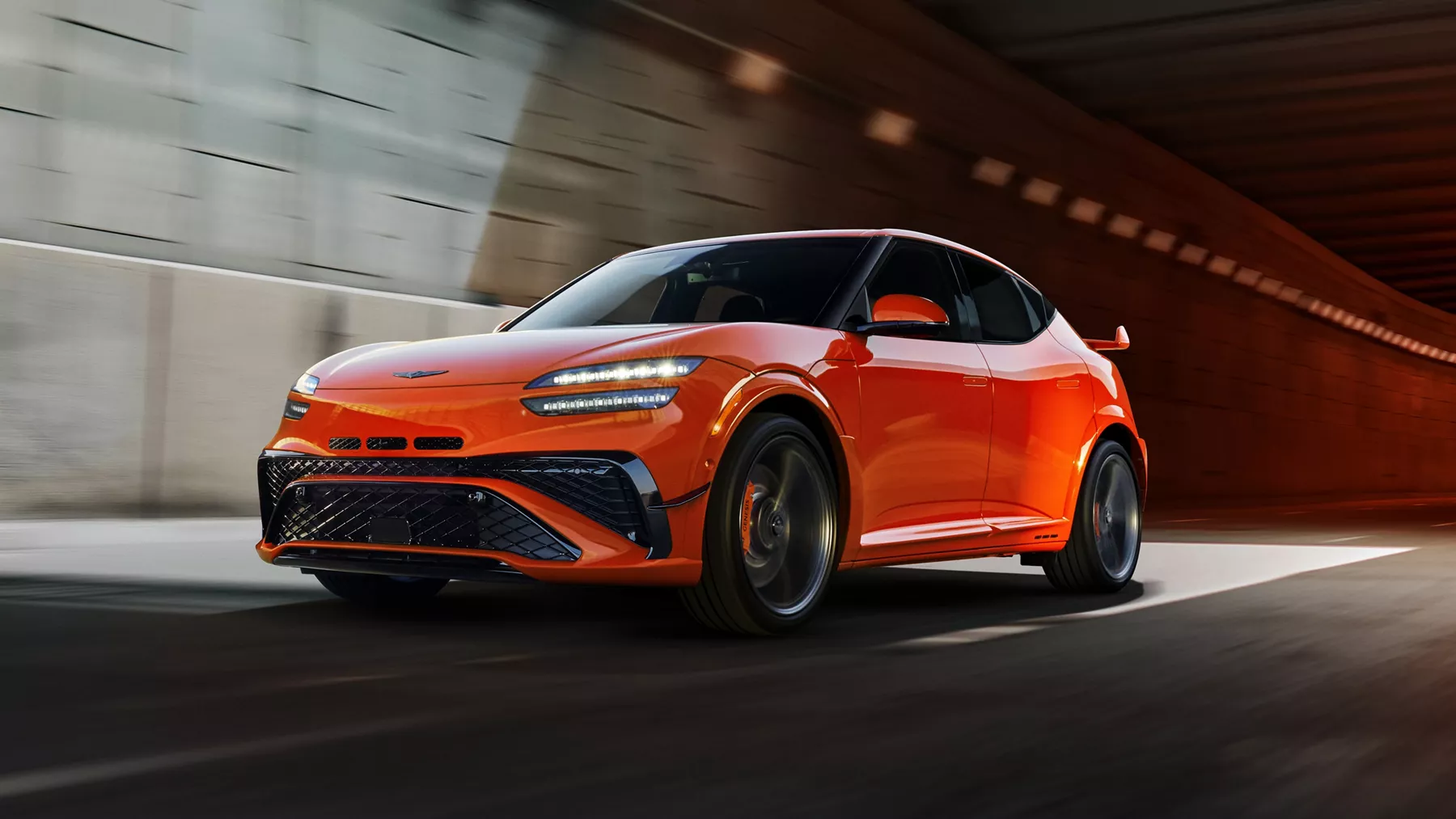 3/4 front driver side view of 2027 Genesis GV60 Magma in orange emerging from tunnel