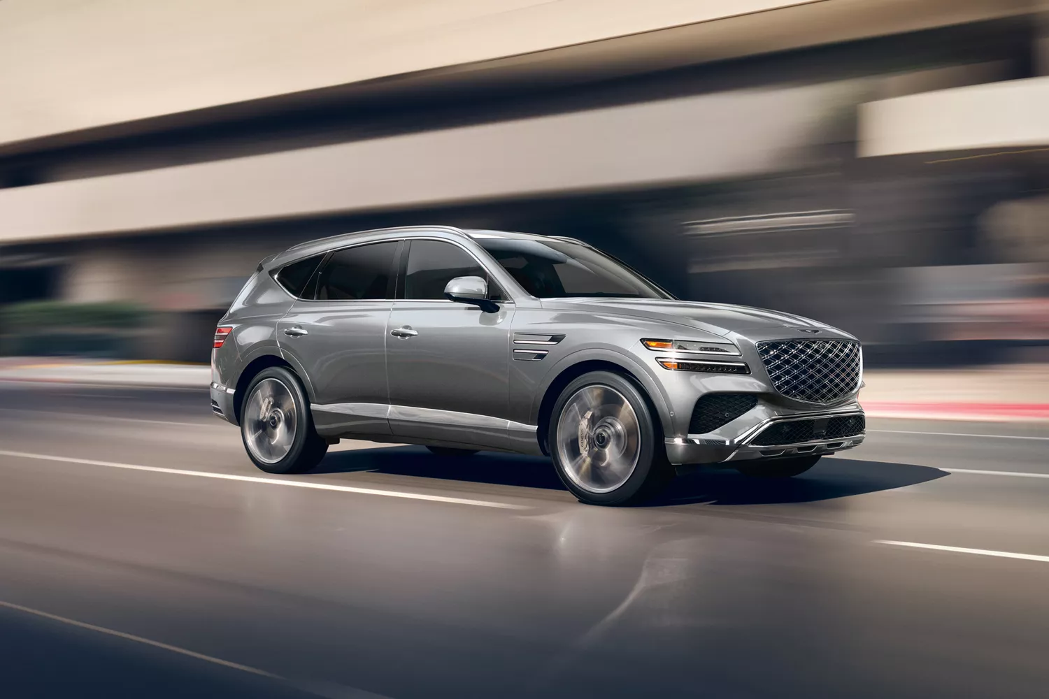 7/8 Front Passenger side view motion blurred Genesis GV80 in Makalu Gray driving on city street
