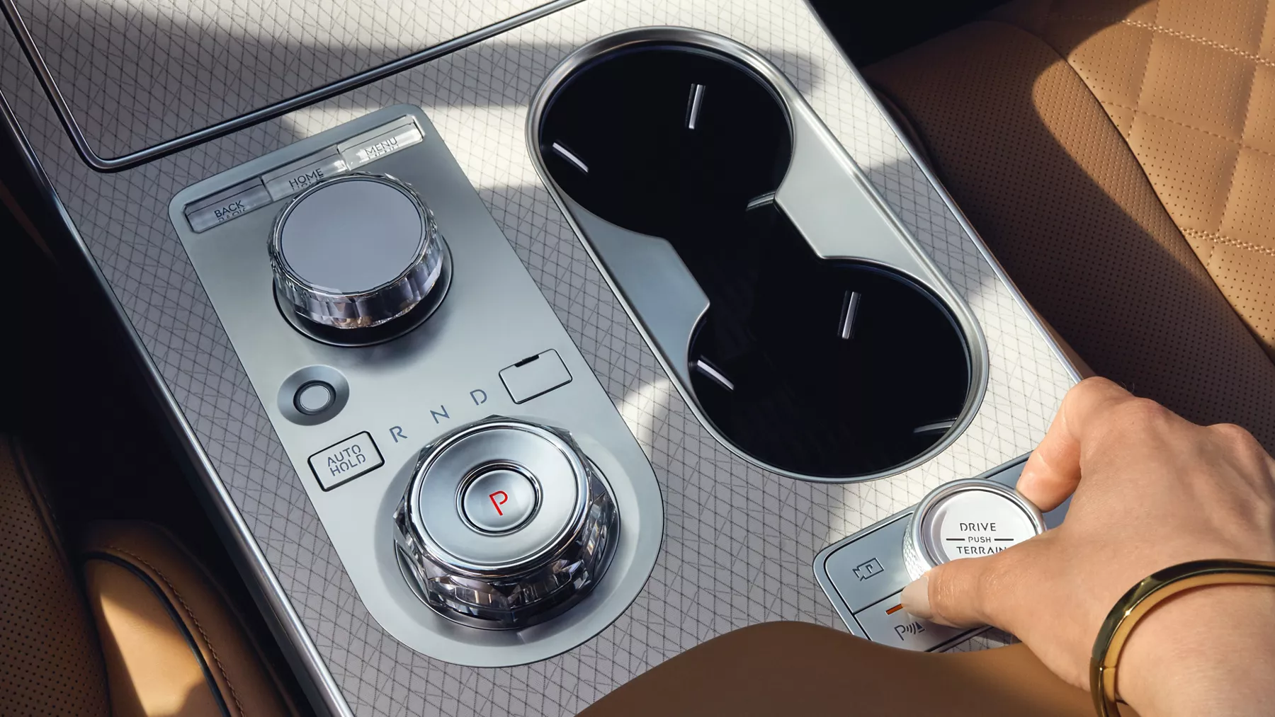Interior closeup of driver's hand holding Drive Mode dial on center console of Genesis GV80
