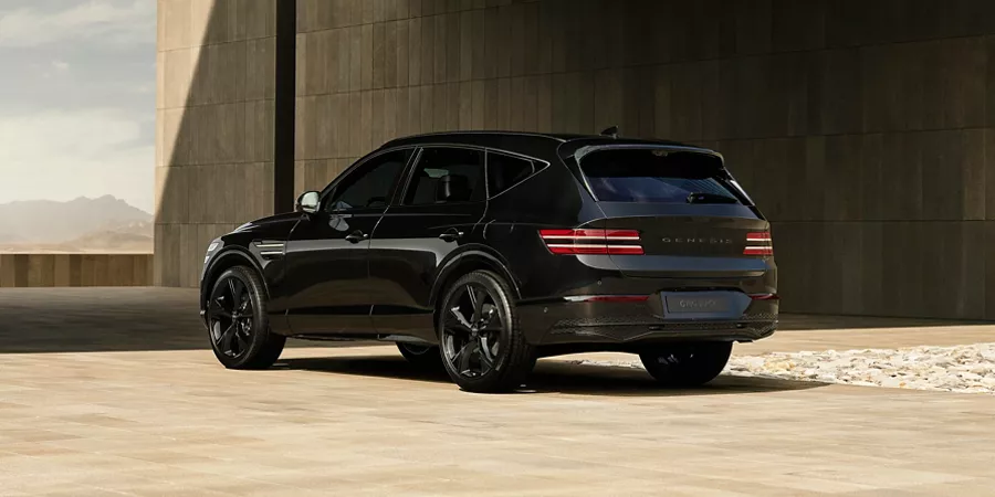 Rear driver side view of Genesis GV80 in Prestige Black parked in front of modern tan building