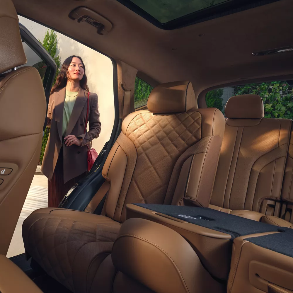 Front driver side POV of Genesis GV80 rear interior with tan quilted leather seats & open rear door