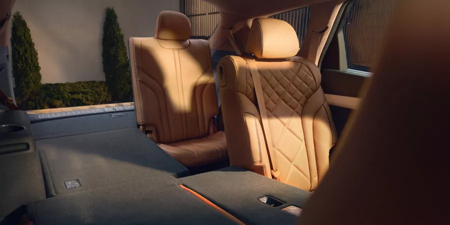 Interior front seat pov of Dune tan leather rear seats folded up on passenger side of Genesis GV80