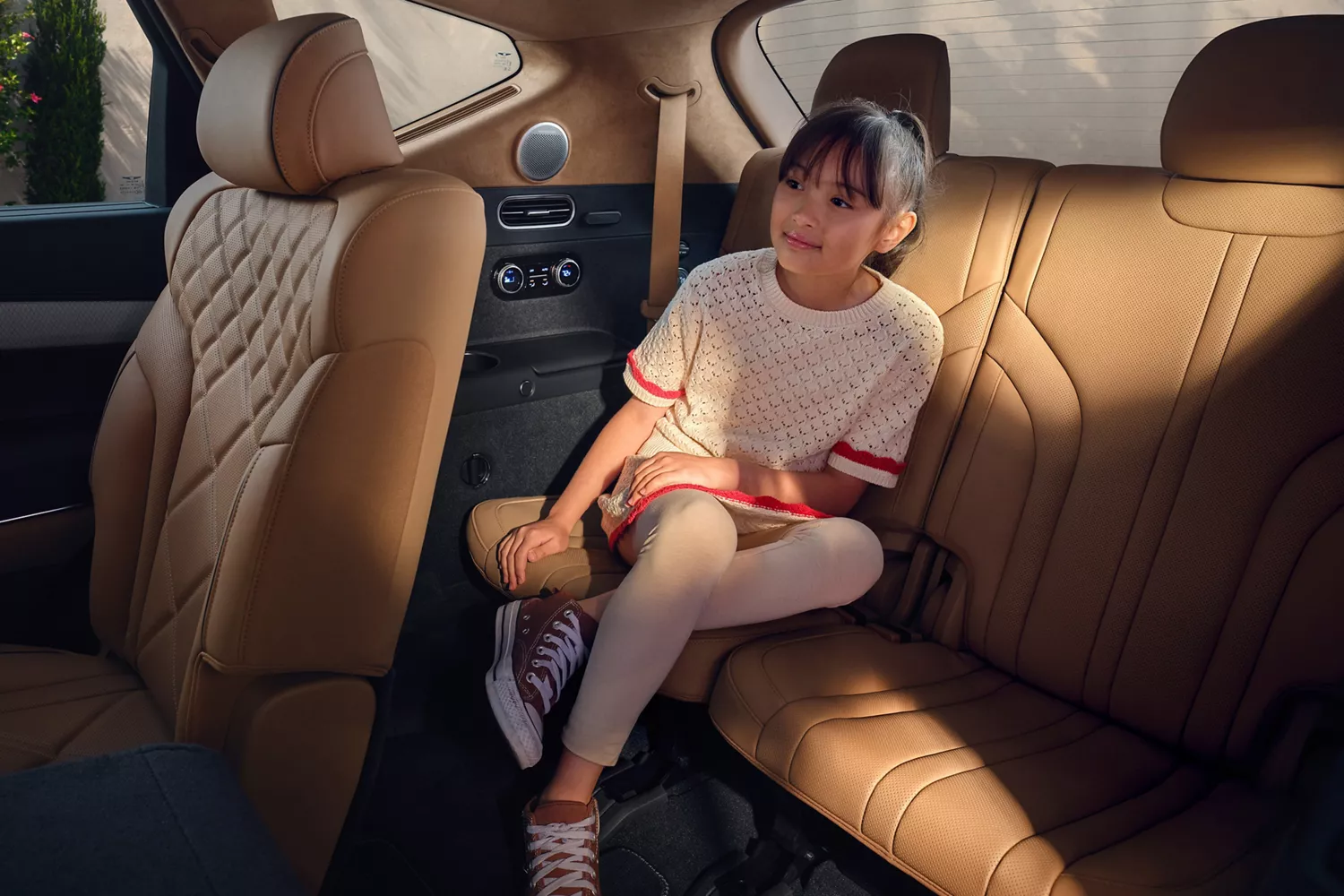 Interior view of child seated in rear Dune tan quilted Nappa leather seats of Genesis GV80
