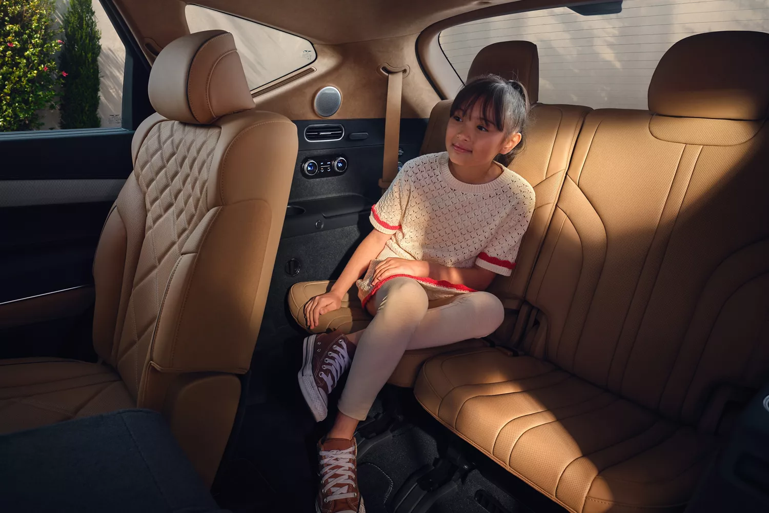 Interior backseat view of child passenger sitting inside Genesis GV80 with tan leather seats