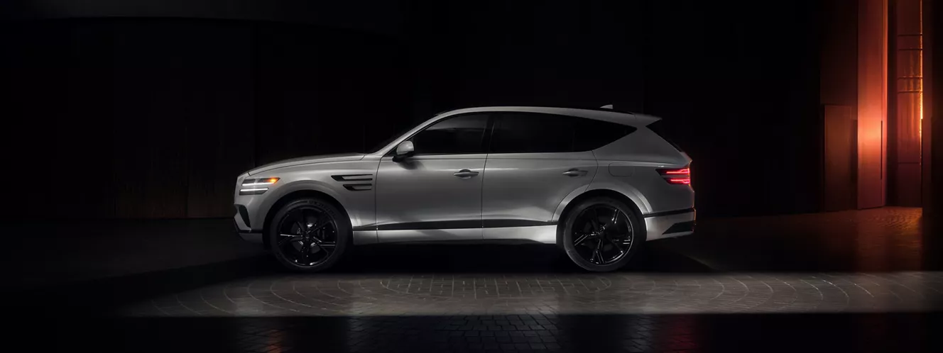 Driver side profile view of Genesis GV80 Prestige Black in Uyuni White parked in dimly lit space