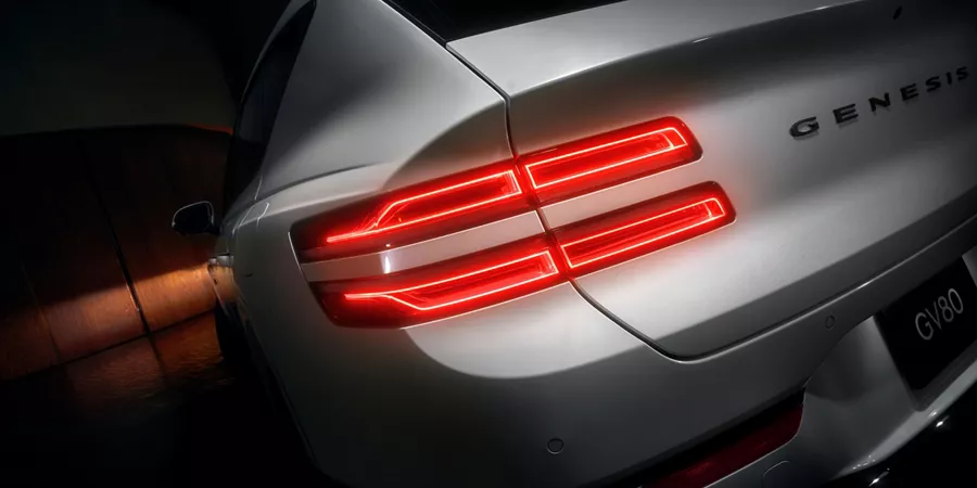 Close up of rear driver side taillight on Genesis GV80 in white, parked in dark space