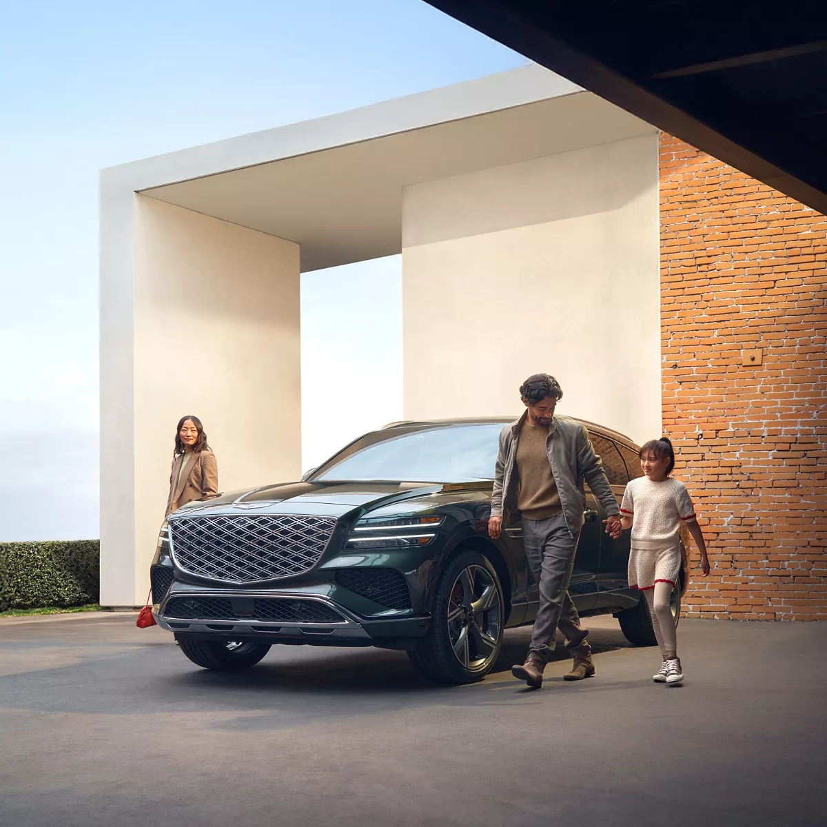 3/4 front driver side view of 2026 Genesis GV80 in Ceres Blue with family walking next to vehicle