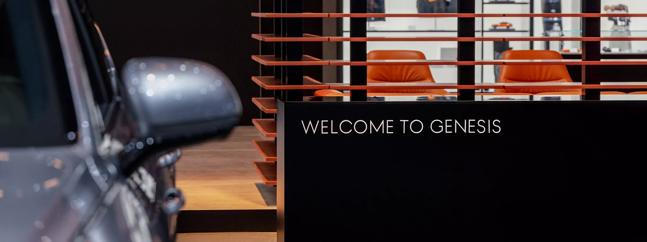 Close up of Genesis GV80 side mirror at 2025 LA Auto Show with 'Welcome to Genesis' sign in background