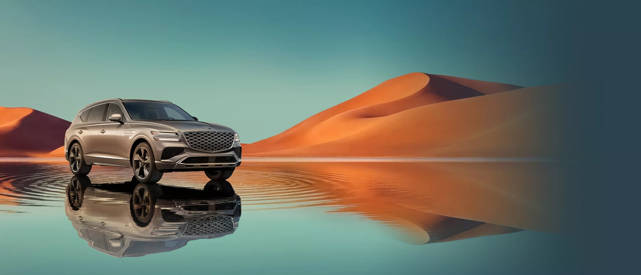 7/8 front passenger view of Savile Silver Genesis GV80 on blue lake w/ orange mountain in background