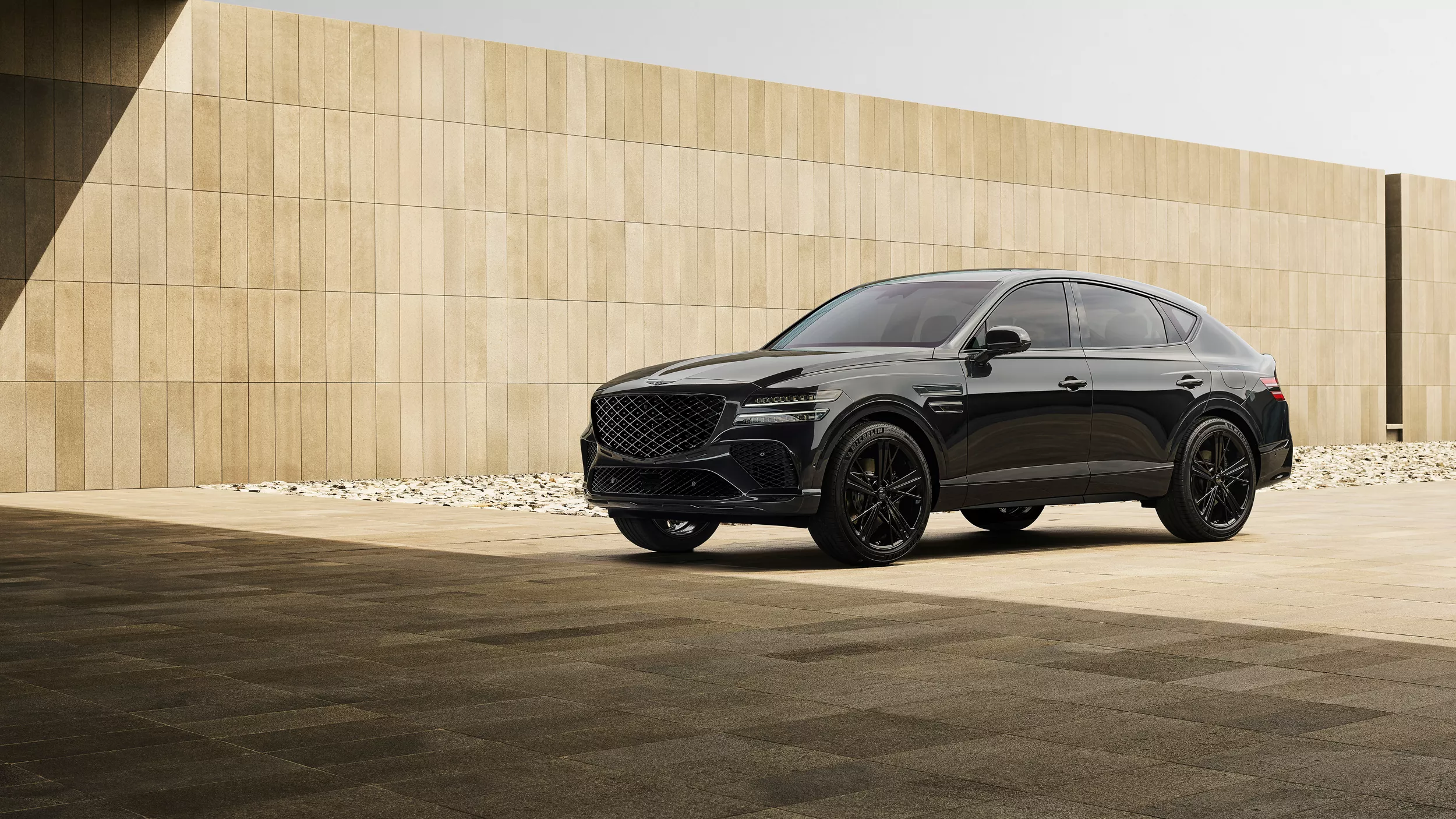 3/4 front driver side view of Genesis GV80 Coupe Prestige Black parked next to beige stone wall