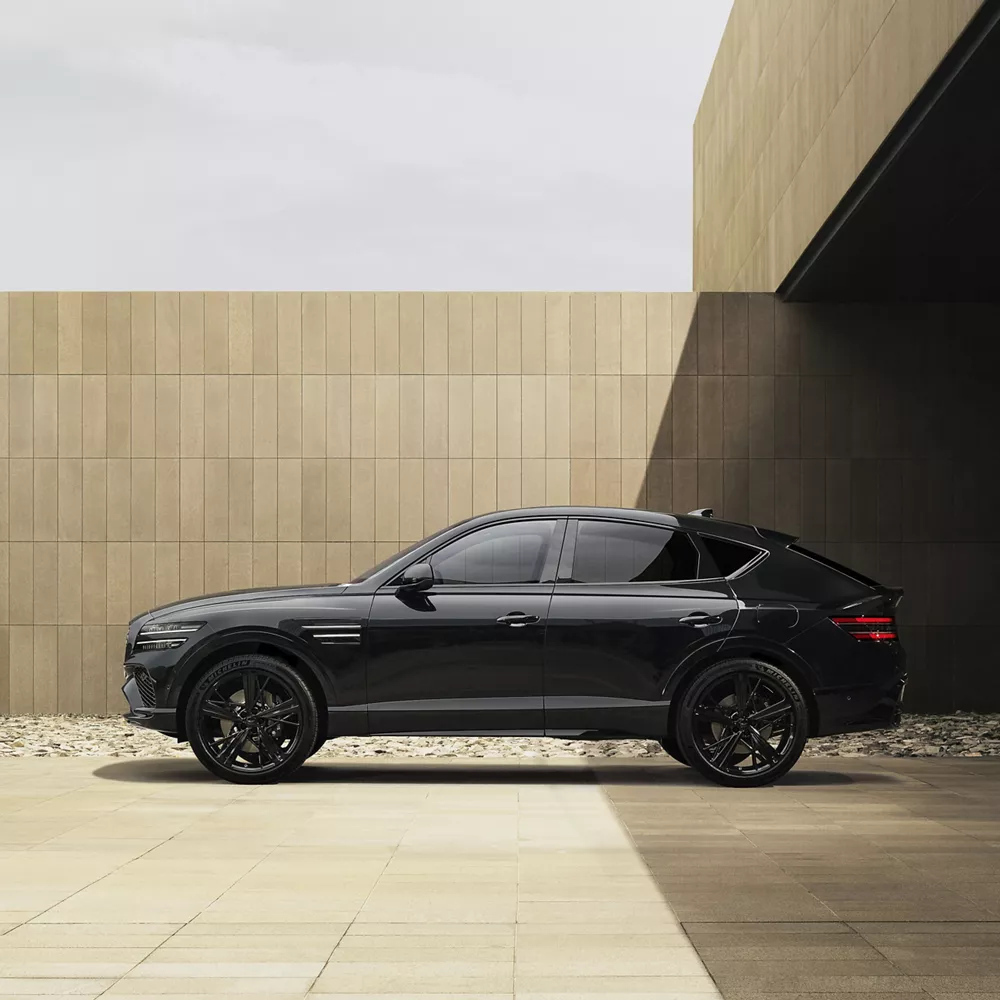 Driver side profile view of 2026 Genesis GV80 Coupe Prestige Black parked outside modern building